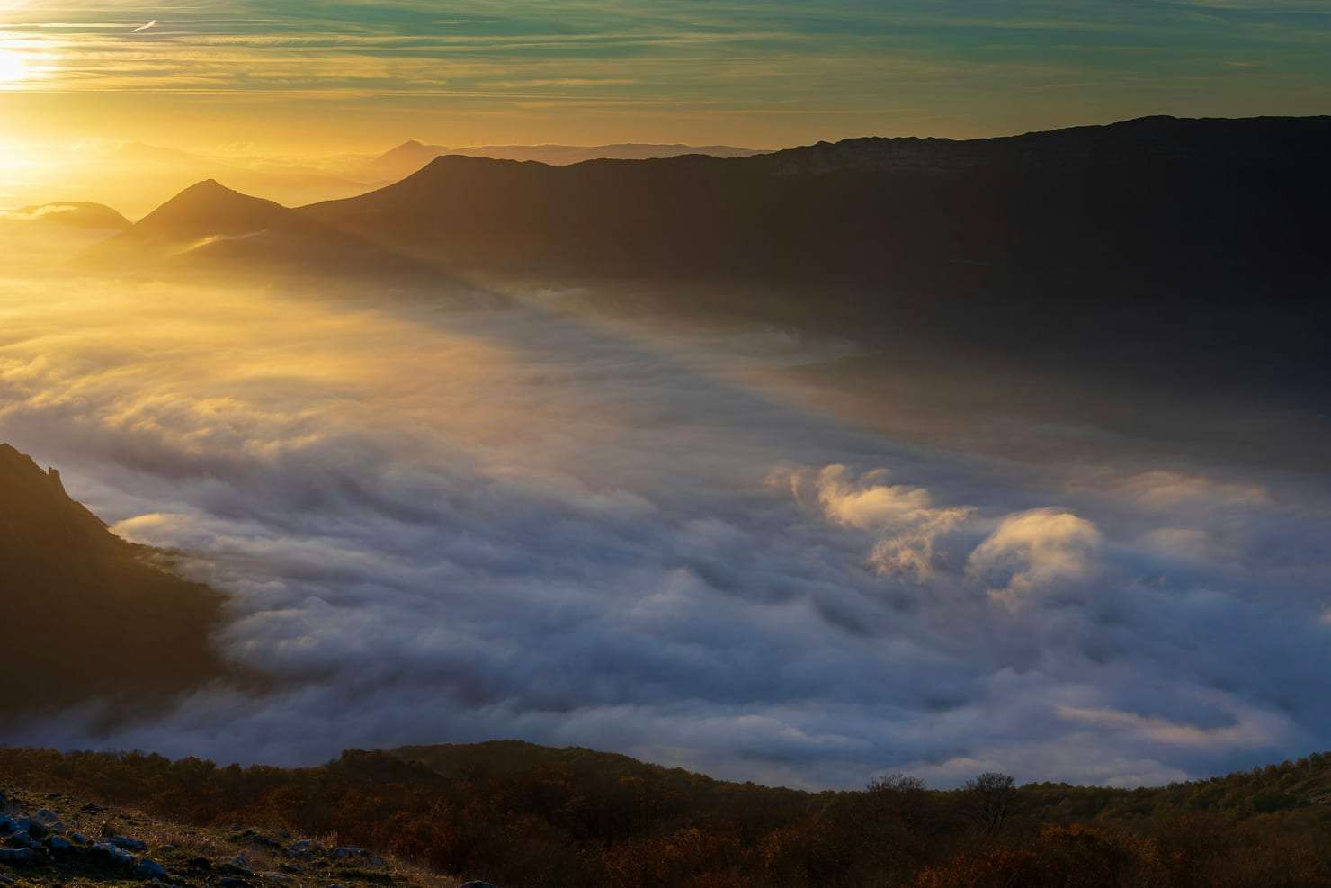Golden sunrise over a quiet misty valley with dark mountain silhouettes.