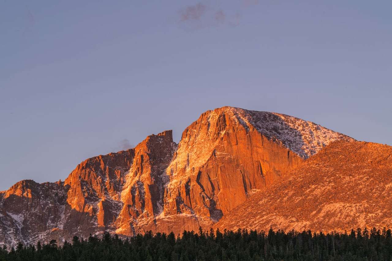 A warm pink mountain summit lit by golden hour sunlight.