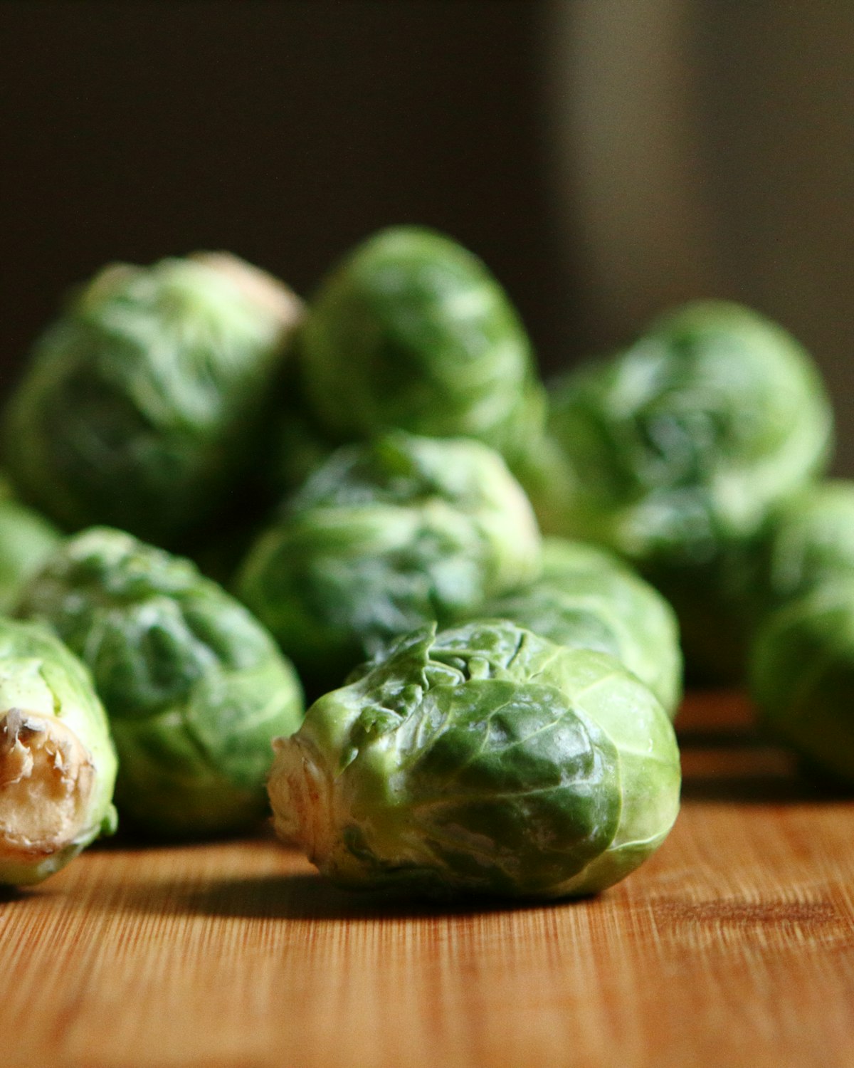 A loose pile of fresh brussels sprouts on a wooden board, lit by low warm light.